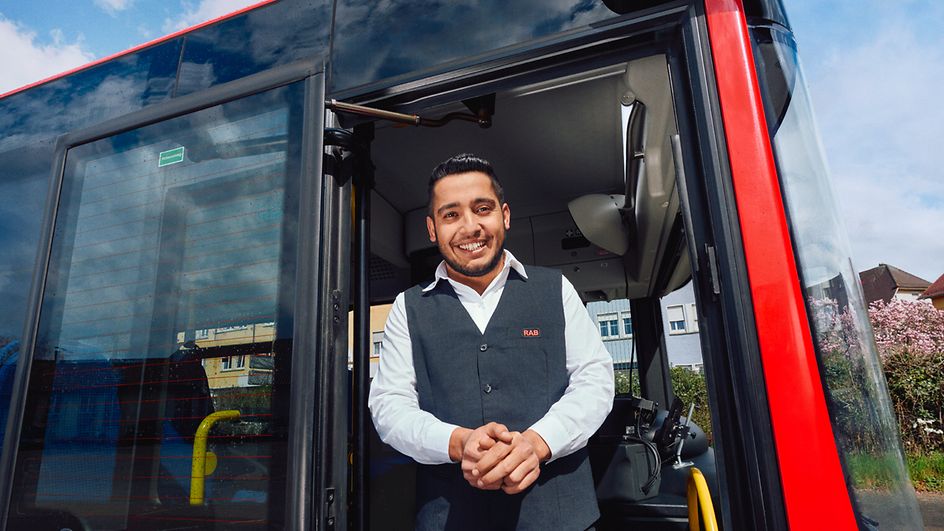 Ein Busfahrer steht in Unternehmensbekleidung am Eingang eines Busses