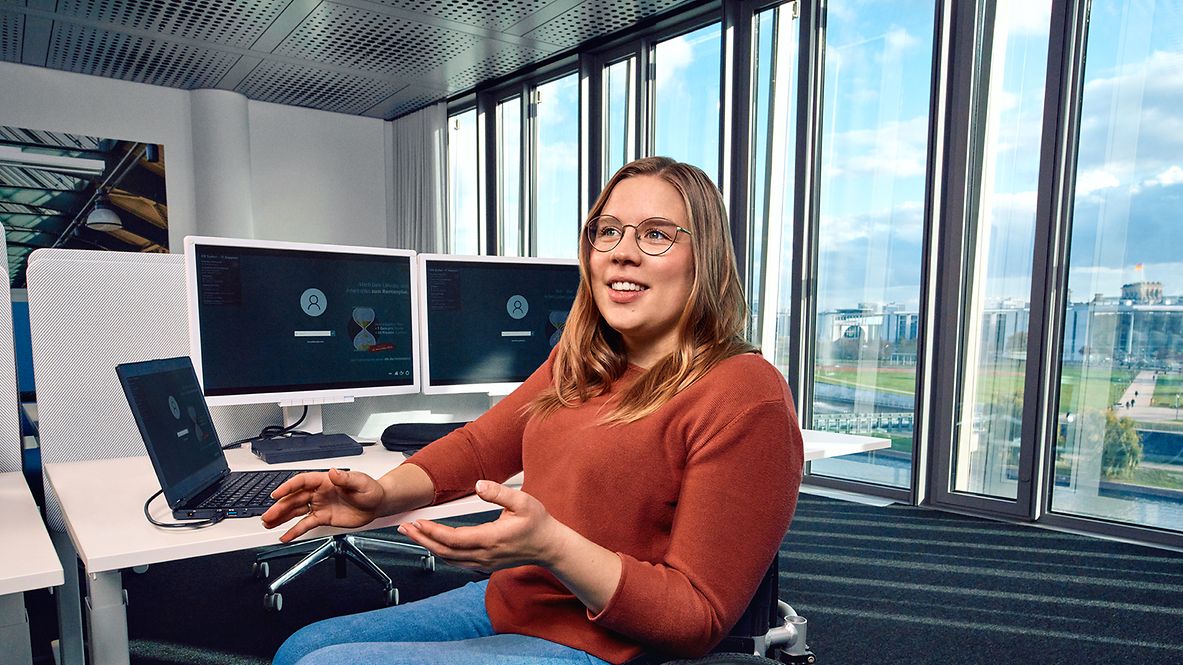 Eine Trainee Inbetriebnahme sitzt im Rollstuhl an ihrem Arbeitsplatz und erklärt etwas