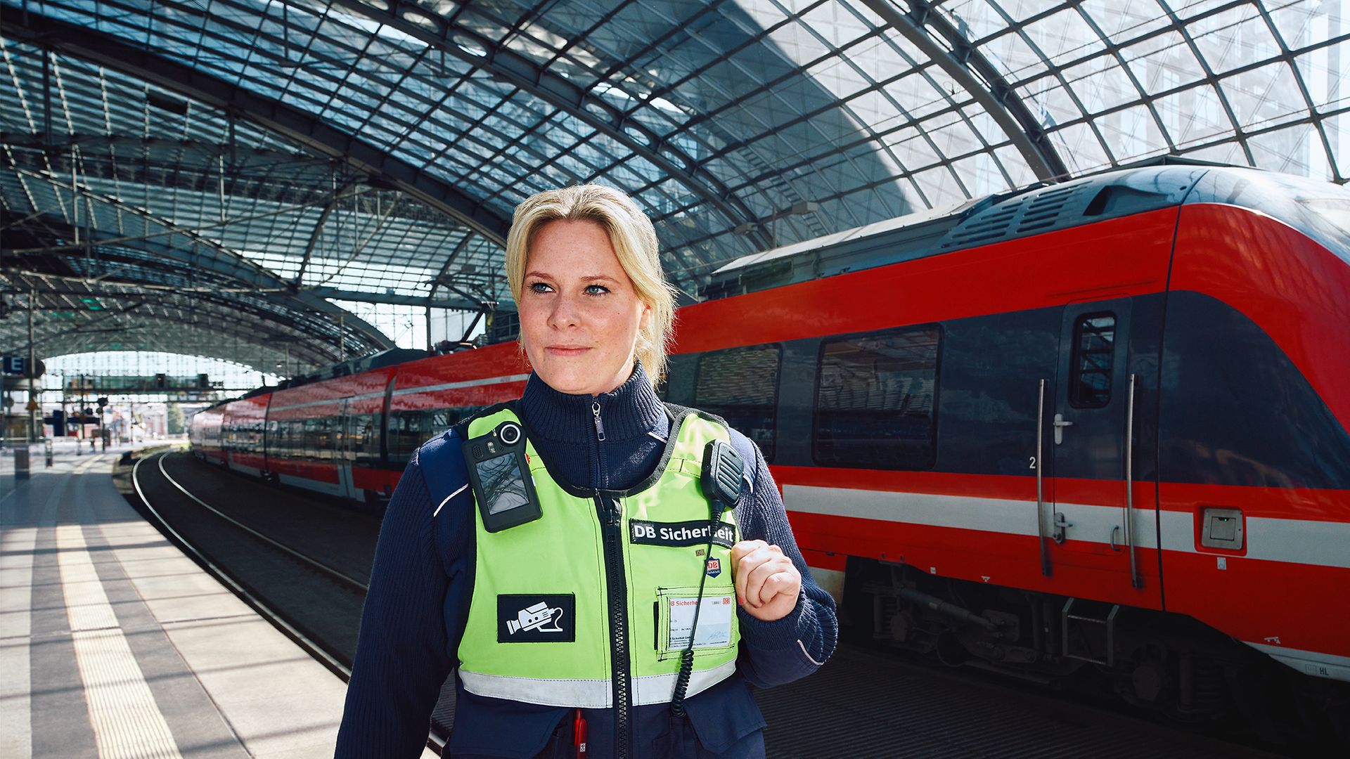 Eine Fachkraft für Schutz und Sicherheit in Unternehmensbekleidung läuft am Bahnsteig eines Bahnhofs an einem Regionalzug vorbei