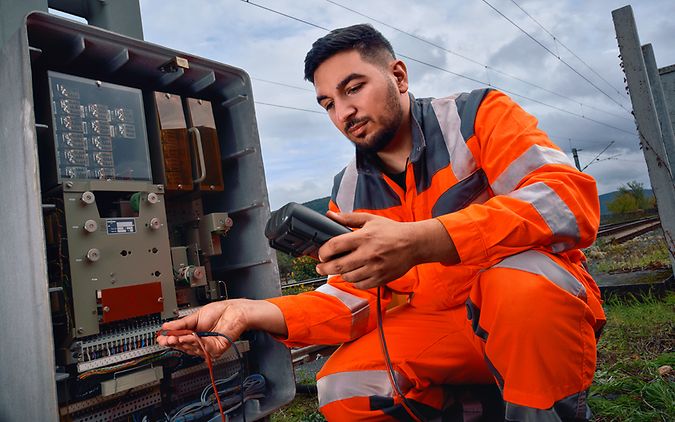 Ein Signalmechaniker steht an eine Sicherungsrelais an der Strecke und führt eine Diagnose mit einem elektronischen Gerät durch