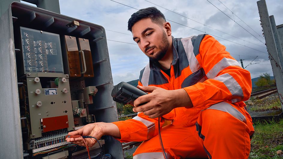 Ein Signalmechaniker steht an eine Sicherungsrelais an der Strecke und führt eine Diagnose mit einem elektronischen Gerät durch