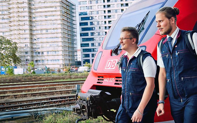 Ein Lokführer und ein Auszubildender gehen an einer Regionalbahn vorbei.