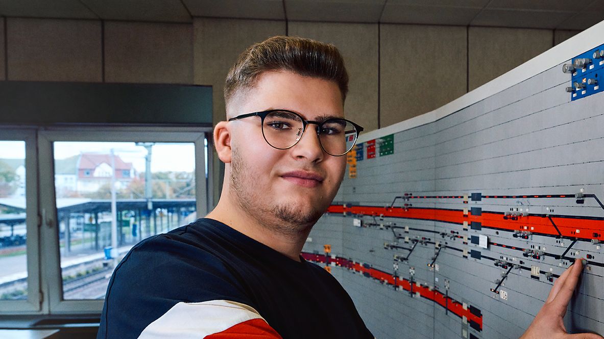 Ein Auszubildender zum Zugverkehrssteuerer steht vor einem Spurplan im Relaisstellwerk