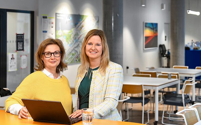 Zwei weibliche Führungskräfte stehen in einem Büro vor einem Laptop