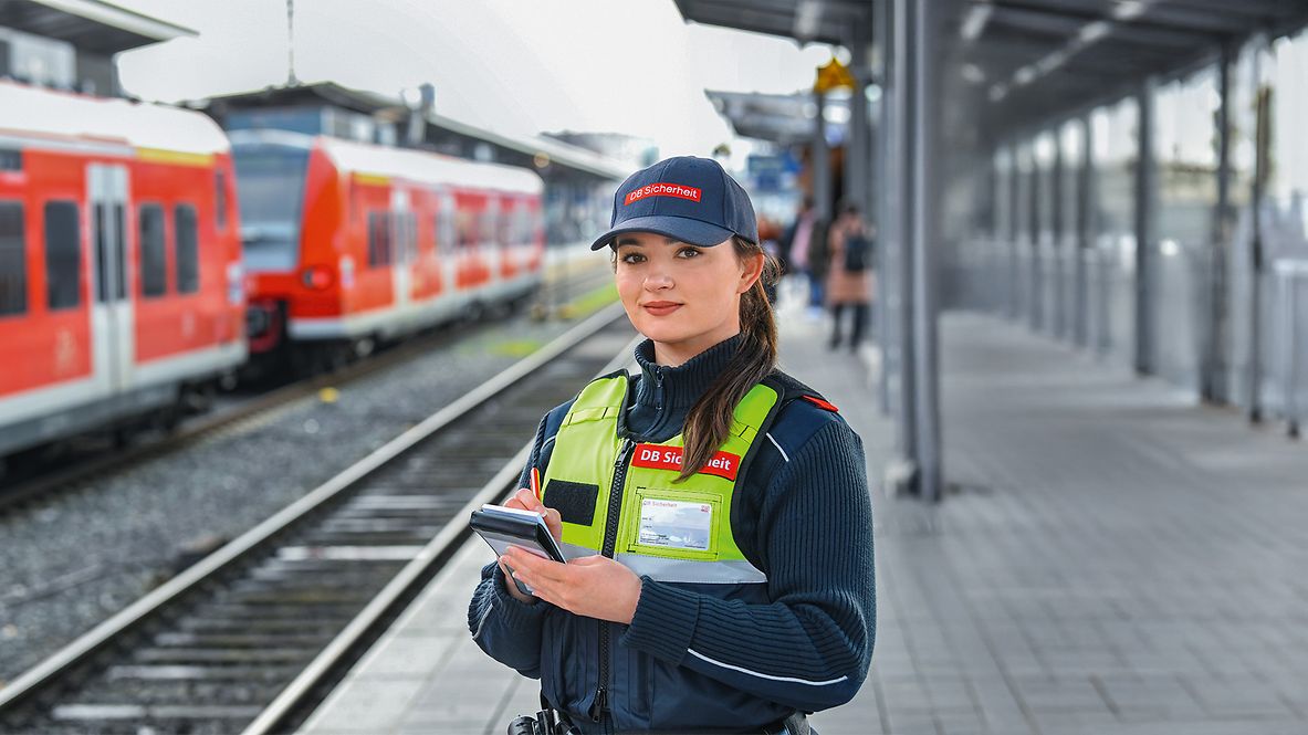 Eine weibliche Fachkraft für Schutz und Sicherheit steht in Unternehmensbekleidung auf dem Bahnhof am Gleis
