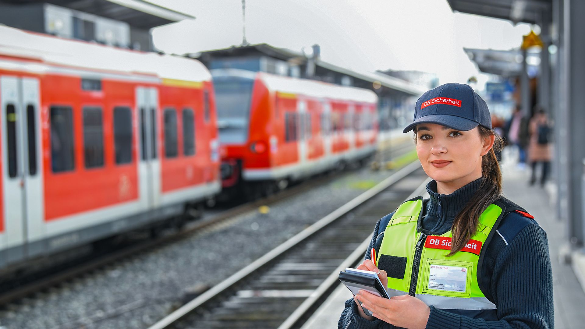Eine weibliche Fachkraft für Schutz und Sicherheit steht in Unternehmensbekleidung auf dem Bahnhof am Gleis