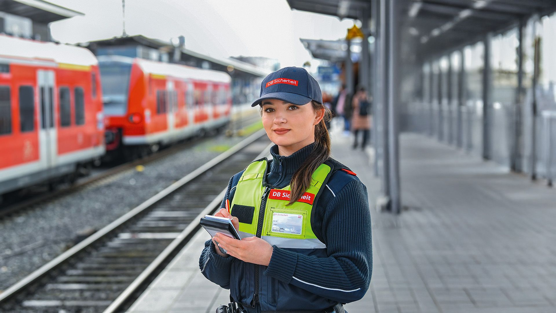 Eine weibliche Fachkraft für Schutz und Sicherheit steht in Unternehmensbekleidung auf dem Bahnhof am Gleis