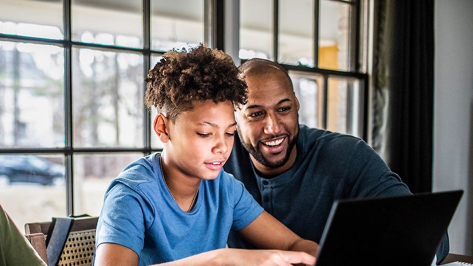 Ein Vater schaut seinem Sohn über die Schulter, während der Sohn am Laptop sitzt