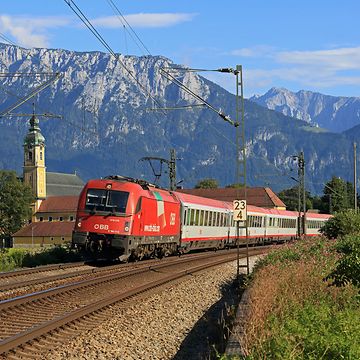 Ein Zug der Österreichischen Bundesbahn ÖBB, im Hintergrund die Berge und eine Kirche