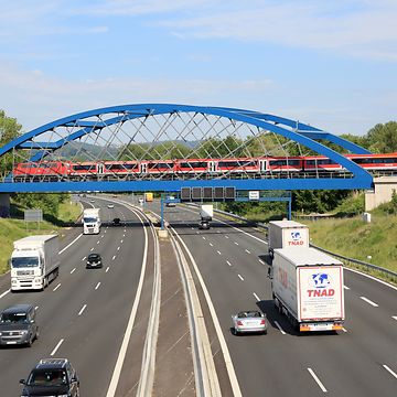 Ein Regionalzug überquert eine blaue Autobahnbrücke