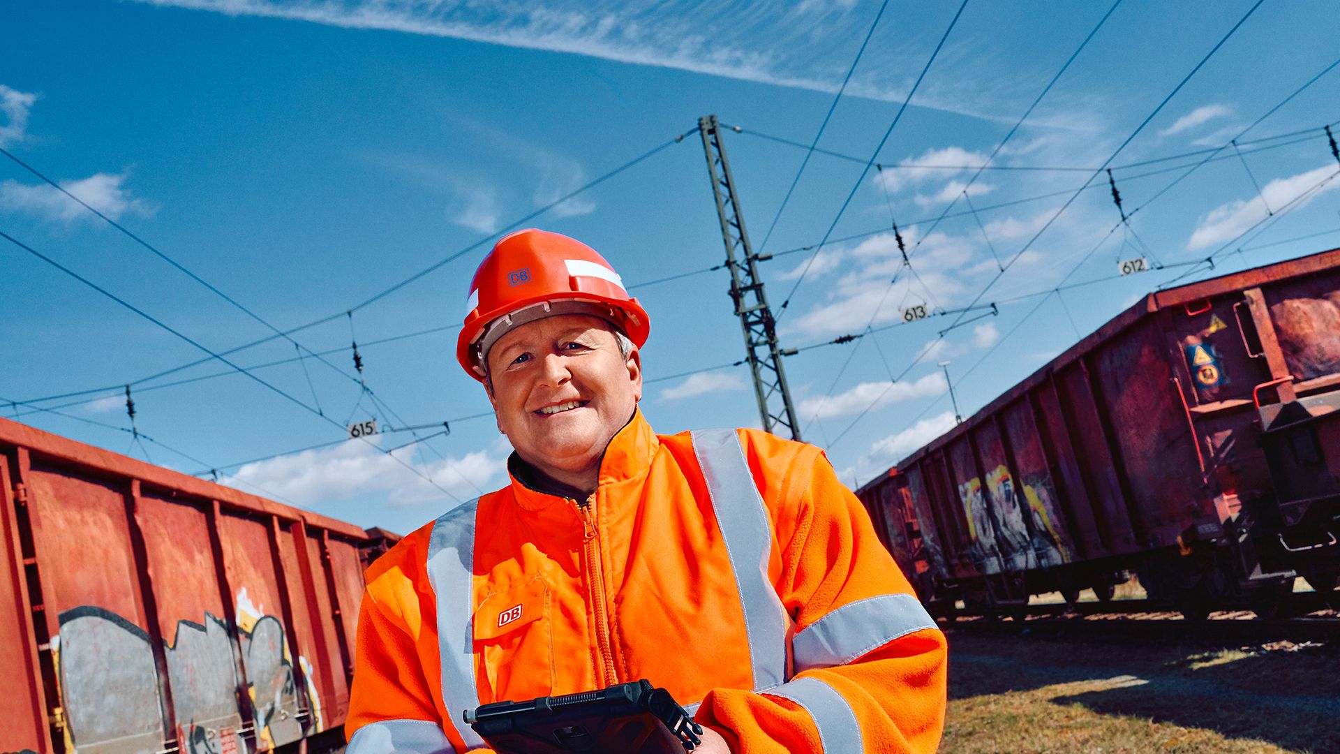 Eine Wagenmeisterin in Warnkleidung und mit Schutzhelm steht zwischen zwei Güterwagons