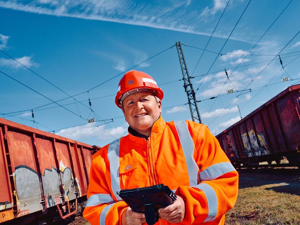 Eine Wagenmeisterin in Warnkleidung und mit Schutzhelm steht zwischen zwei Güterwagons