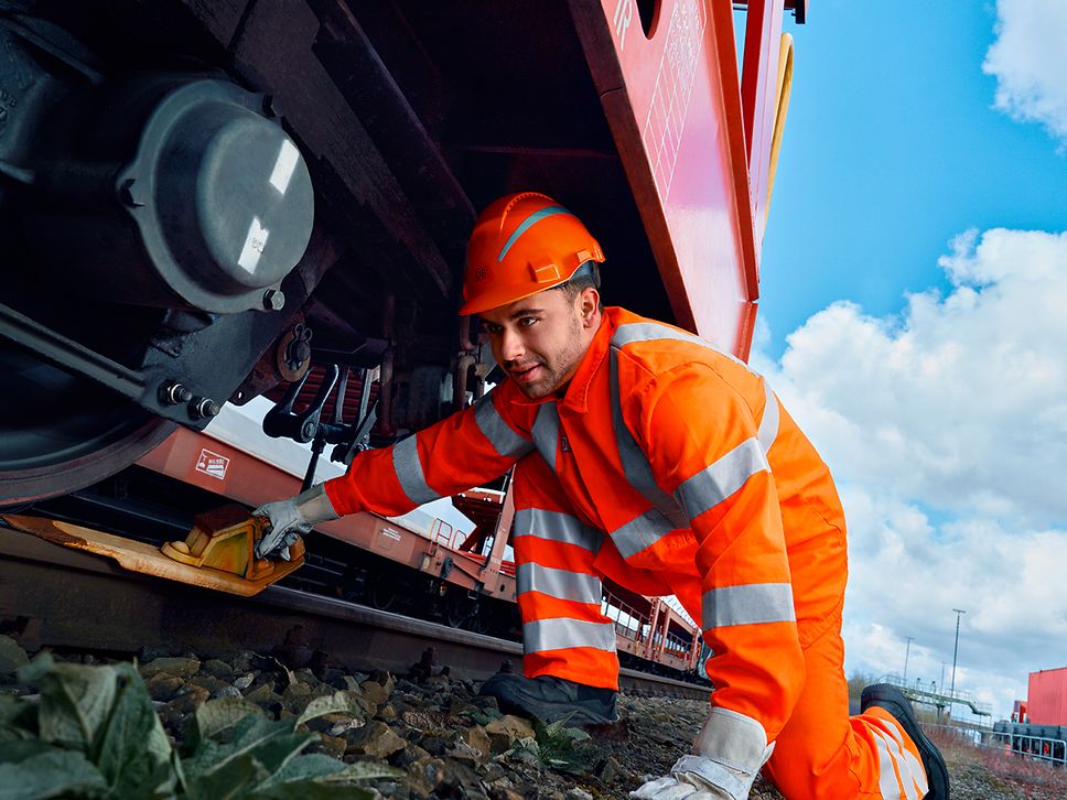 Ein Lokrangierführer in Warnweste und mit Schutzhelm platziert einen Hemmschuh an der Lok