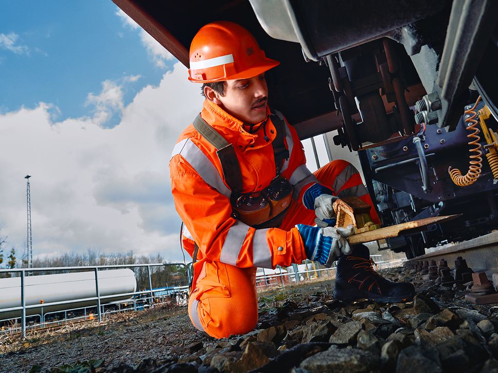 Ein Lokrangierführer in Warnweste und mit Schutzhelm entfernt einen Hemmschuh von der Lok