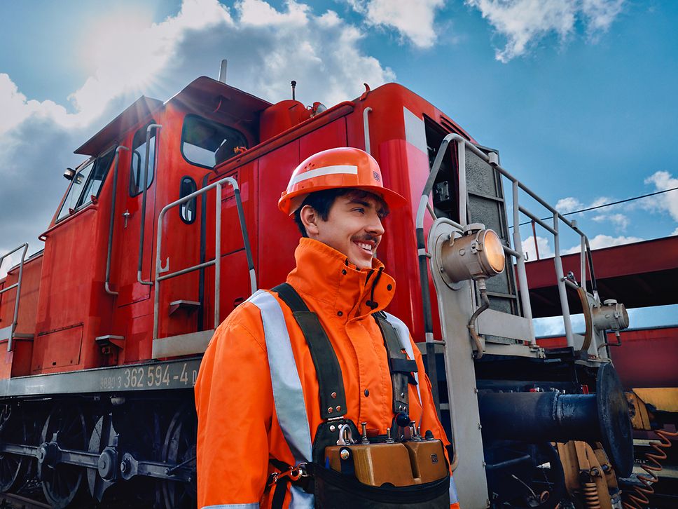 Ein Lokrangierführer in Warnweste und mit Schutzhelm läuft vor einem Triebwagen des Güterverkehrs entlang