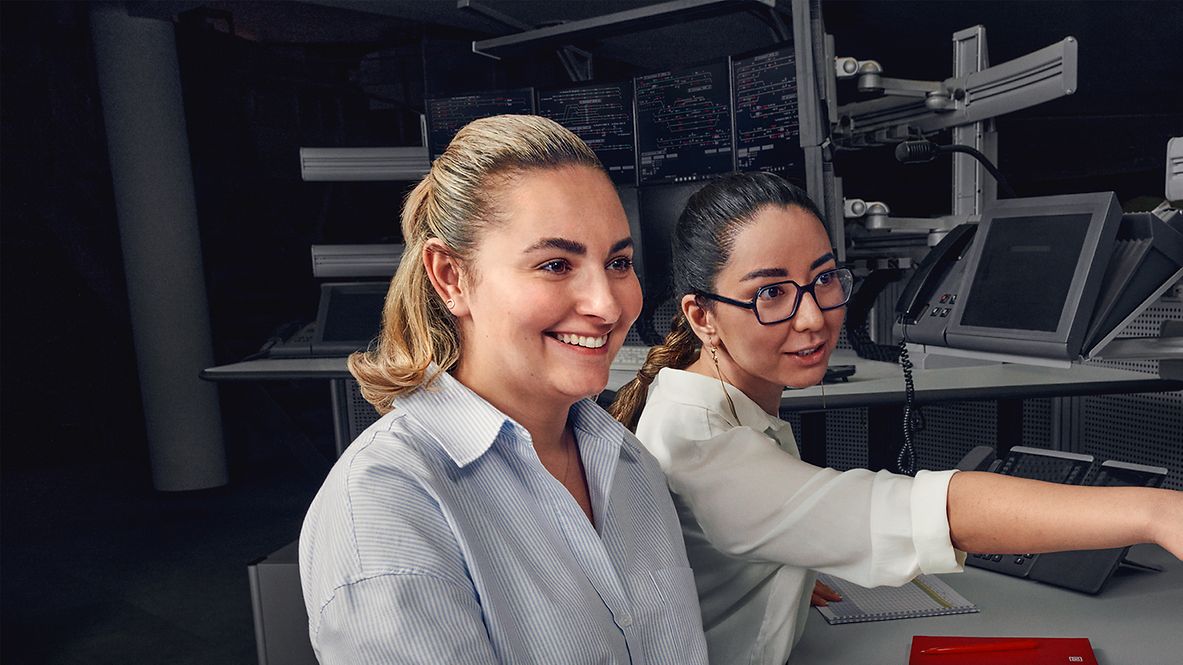 Zwei Fahrdienstleiterinnen sitzen vor den Bildschirmen des elektronischen Stellwerkes, eine von ihnen zeigt auf einen Bildschirm