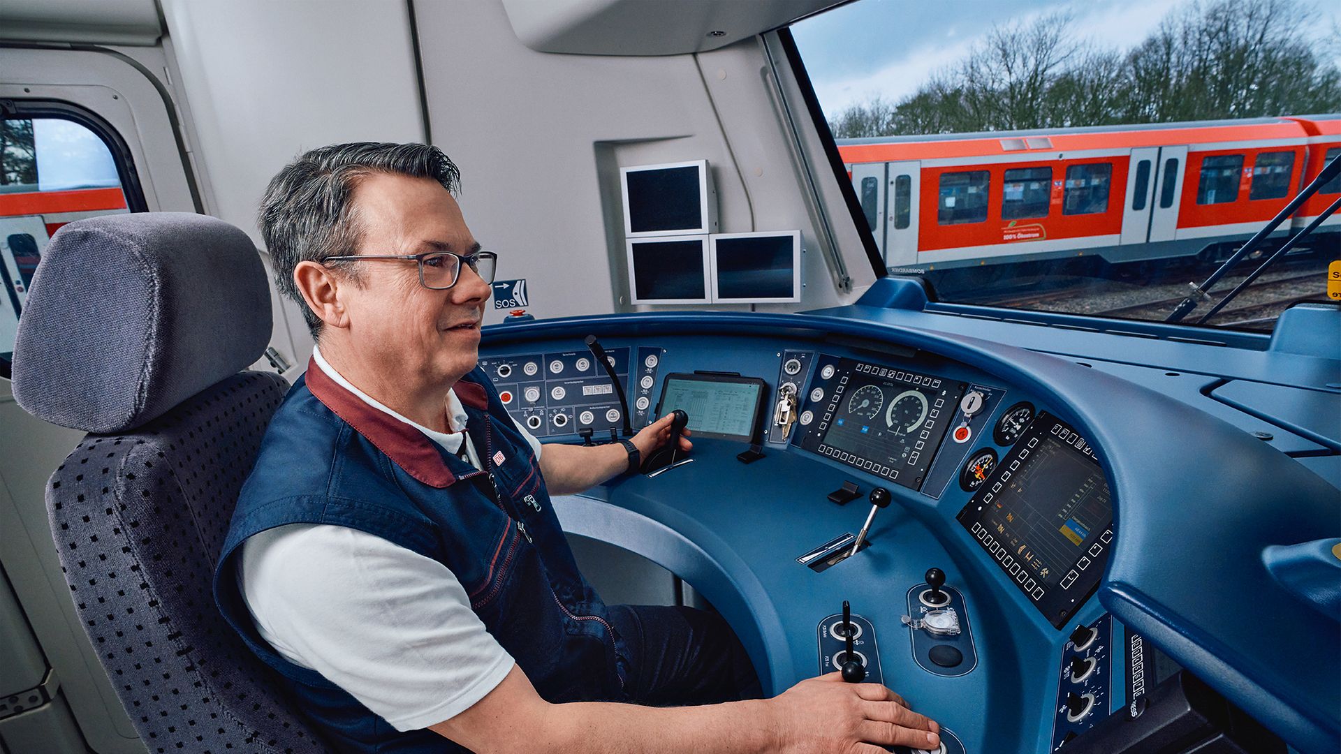 Ein Lokführer der S-Bahn Hamburg sitzt in Unternehmensbekleidung im Führerstand und fährt einen Zug