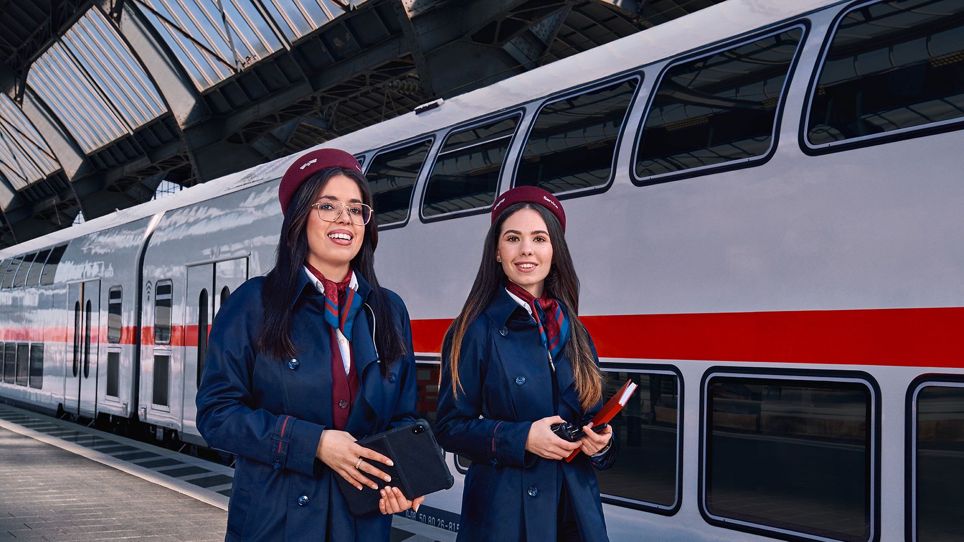 Zwei Auszubildende zur Kauffrau für Verkehrsservice gehen am Bahnsteig eines Bahnhofes an einem Regionalzug vorbei