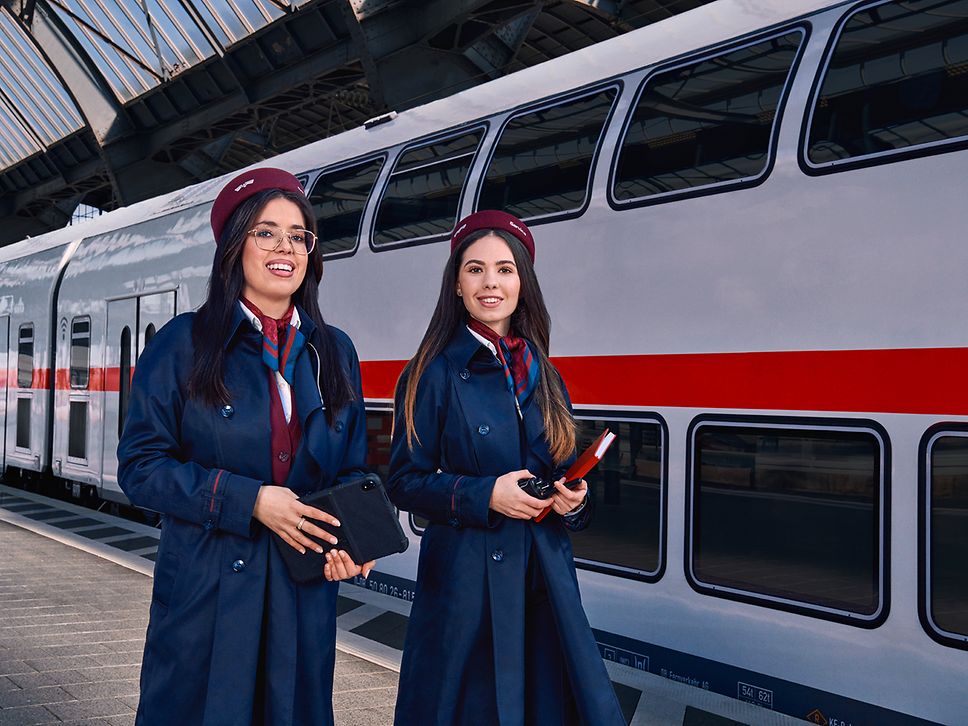 Zwei Auszubildende zur Kauffrau für Verkehrsservice gehen am Bahnsteig eines Bahnhofes an einem Regionalzug vorbei