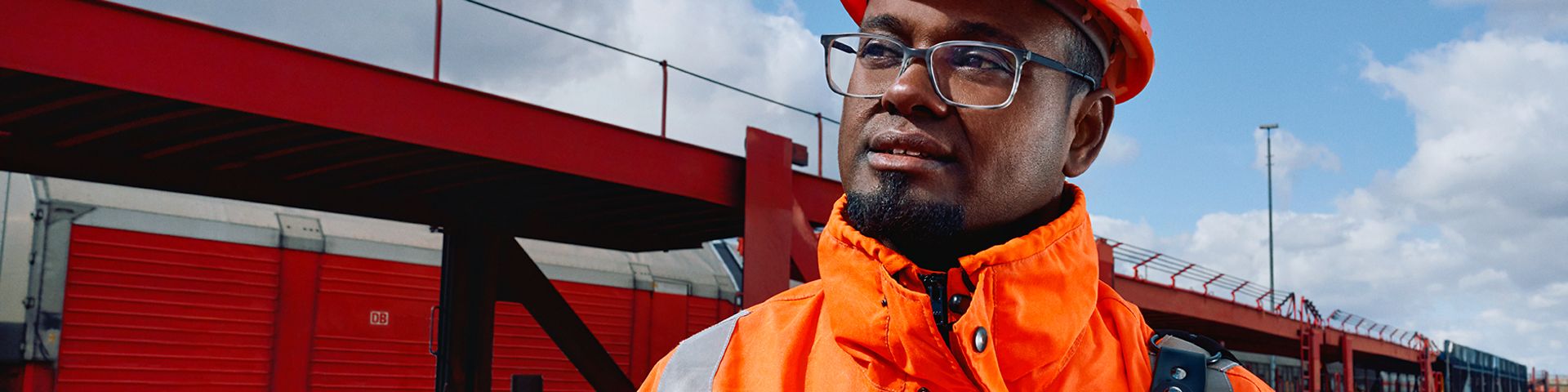 Ein Lokrangierführer in Warnweste und mit Schutzhelm steht vor Güterverkehrszügen