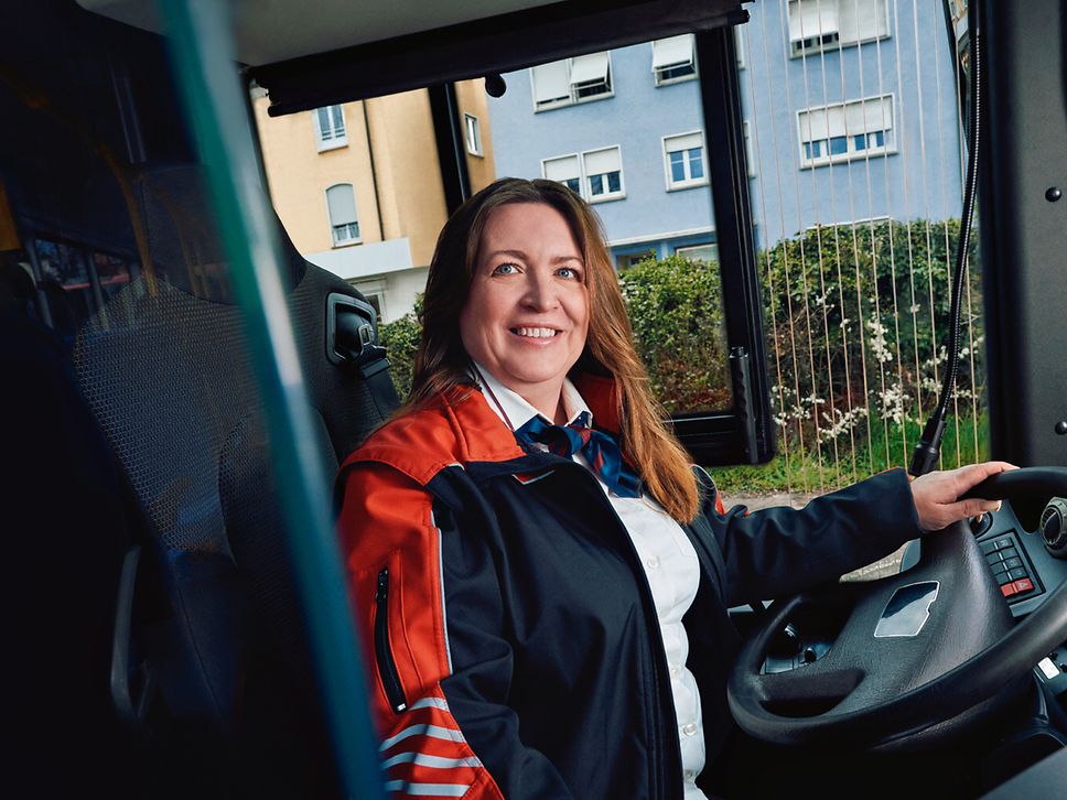 Eine Busfahrerin sitzt in Unternehmensbekleidung am Steuer eines Busses