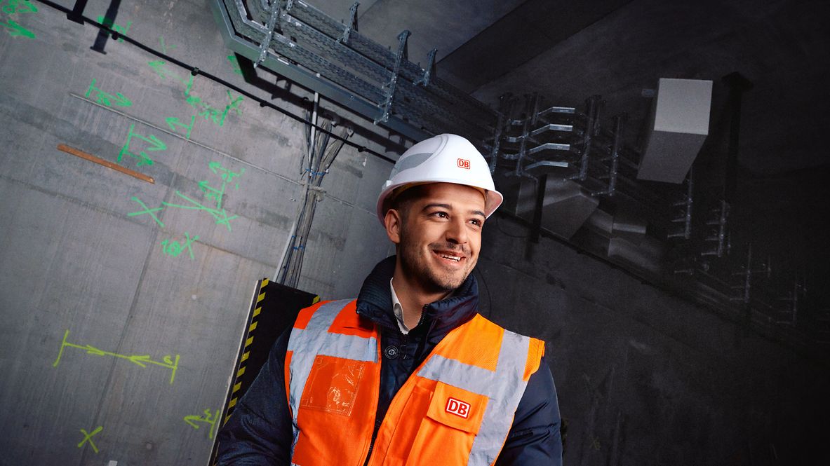 Ein Planungsingenieur steht in Warnkleidung und mit Schutzhelm vor einer Baustelle