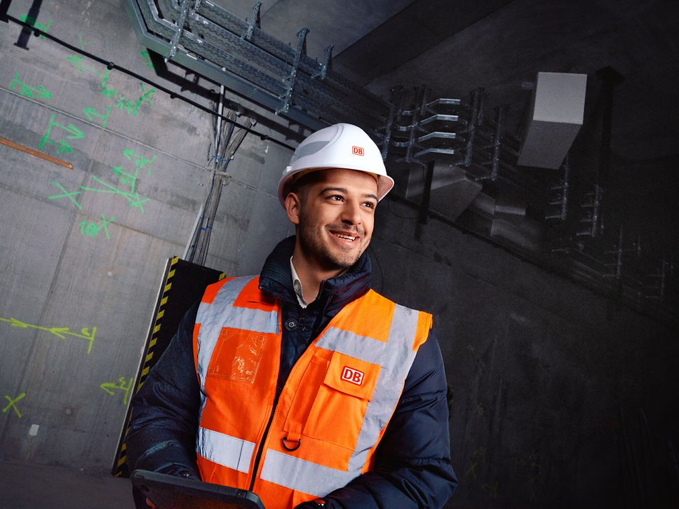 Ein Planungsingenieur steht in Warnkleidung und mit Schutzhelm vor einer Baustelle