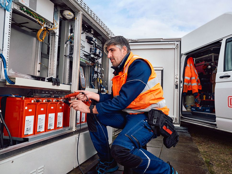 Ein Servicetechniker in Arbeitskleidung und mit Warnweste kniet vor einem Schutzrelaisschrank