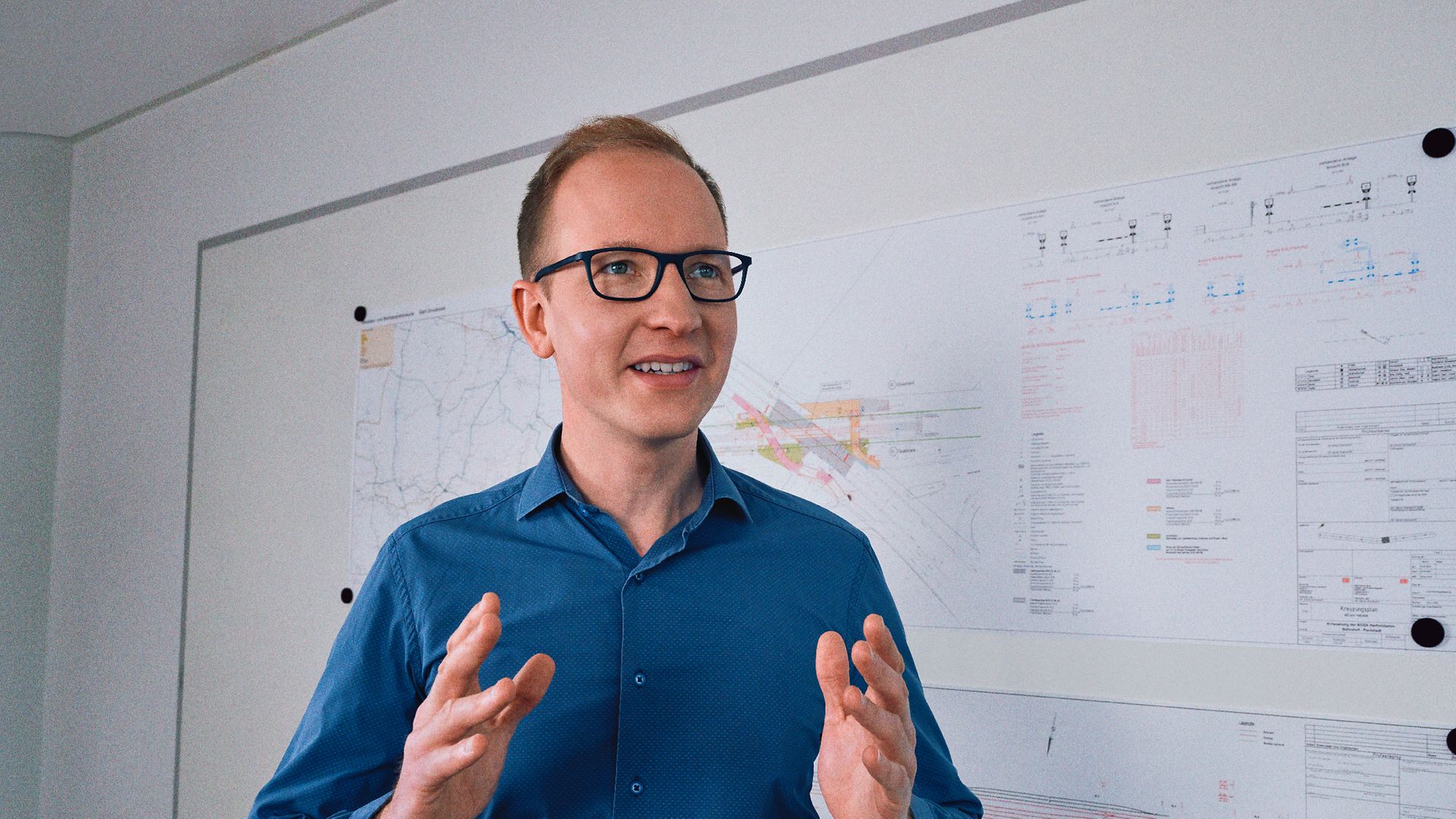 Ein Projektleiter steht in einem Büro vor Planungsunterlagen und erklärt etwas