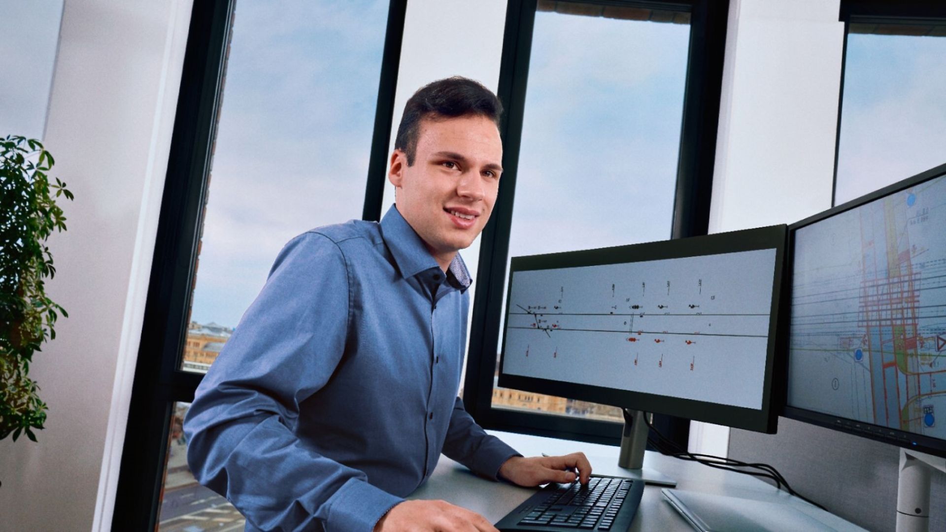 Ein Dualstudierender Elektrotechnik mit Schwerpunkt Leit- und Sicherungstechnik steht an einem Schreibtisch und arbeitet am PC