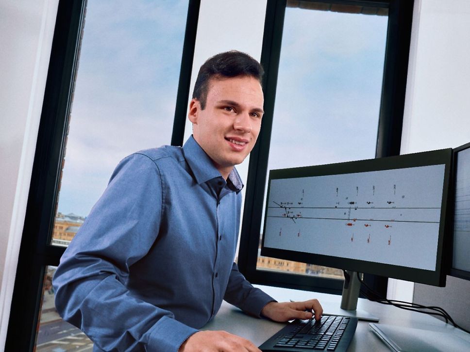 Ein Dualstudierender Elektrotechnik mit Schwerpunkt Leit- und Sicherungstechnik steht an einem Schreibtisch und arbeitet am PC