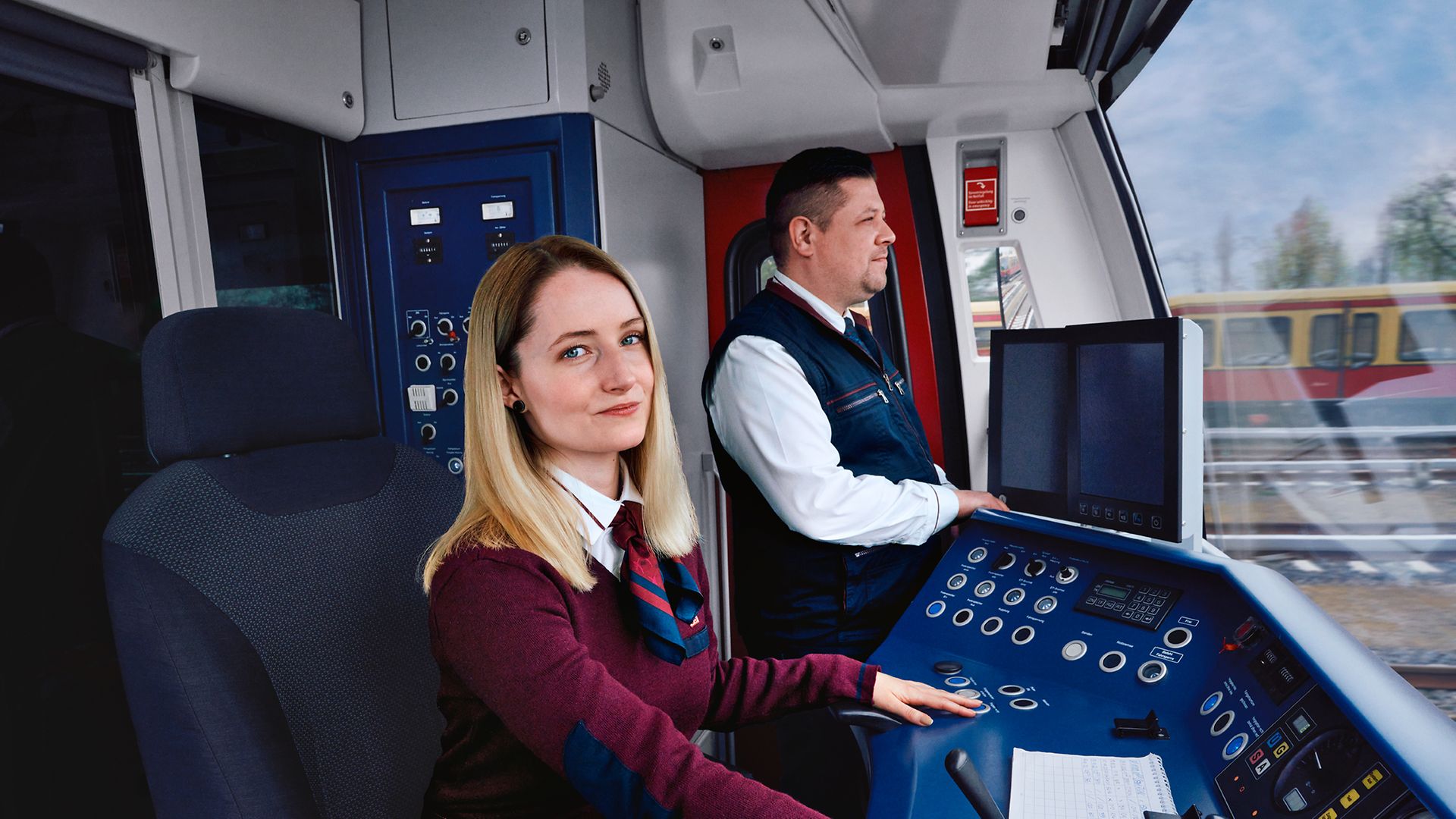 Eine Auszubildende zur Lokführerin sitzt neben einem Ausbilder im Führerstand einer S-Bahn und steuert den Zug