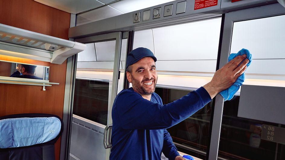 Ein Fahrzeugreiniger in Arbeitskleidung reinigt Abteiltüren im Zug