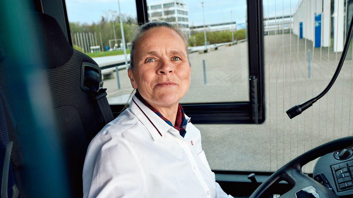 Eine Busfahrerin sitzt in Unternehmensbekleidung am Steuer eines Busses