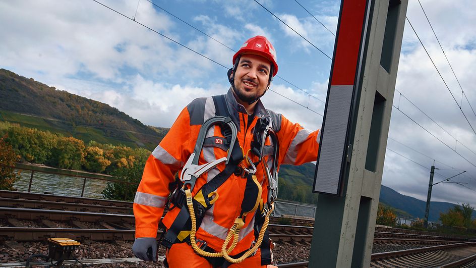 Ein Signalmechaniker in Arbeitskleidung und Schutzausrüstung steht im Gleisbett neben einer Signalanlage