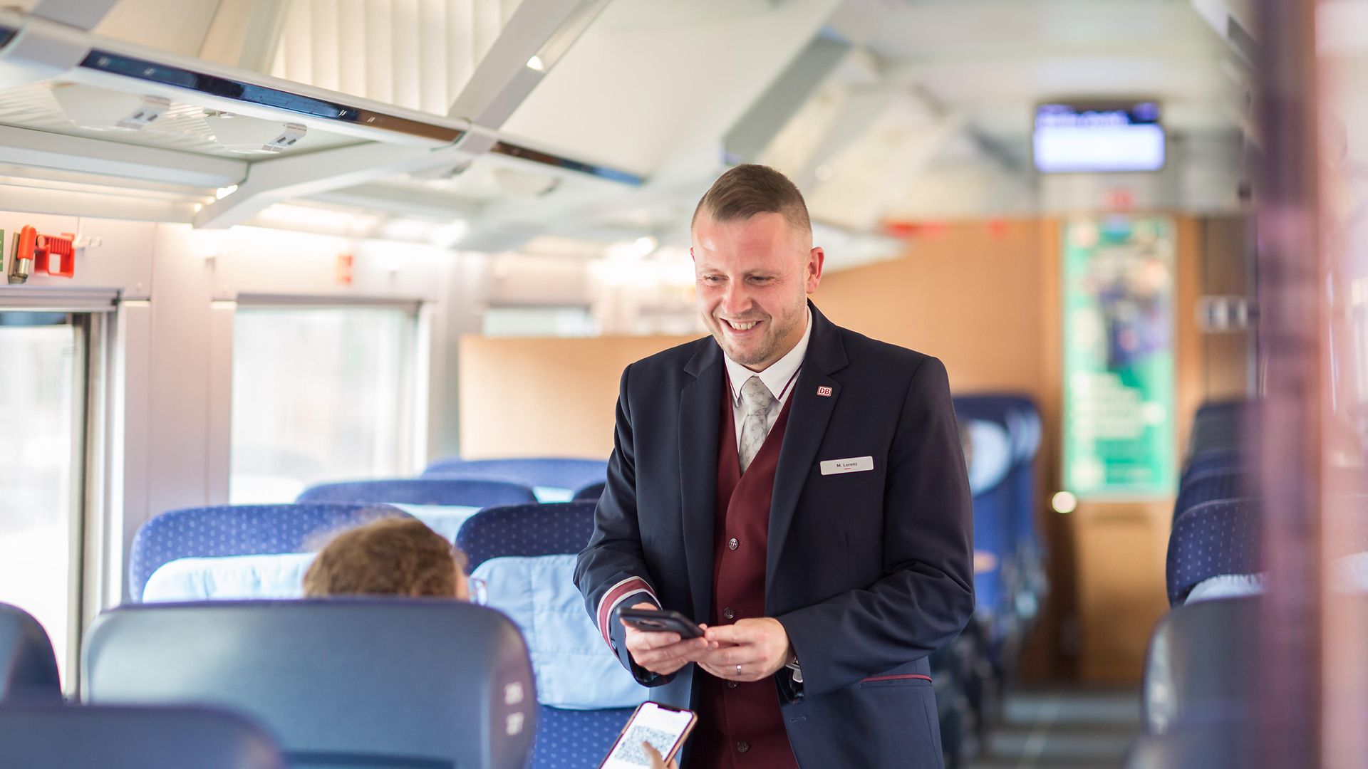Ein Zugchef steht im Gang eines ICE-Zuges und hält ein elektronisches Gerät zur Fahrkartenkontrolle in der Hand