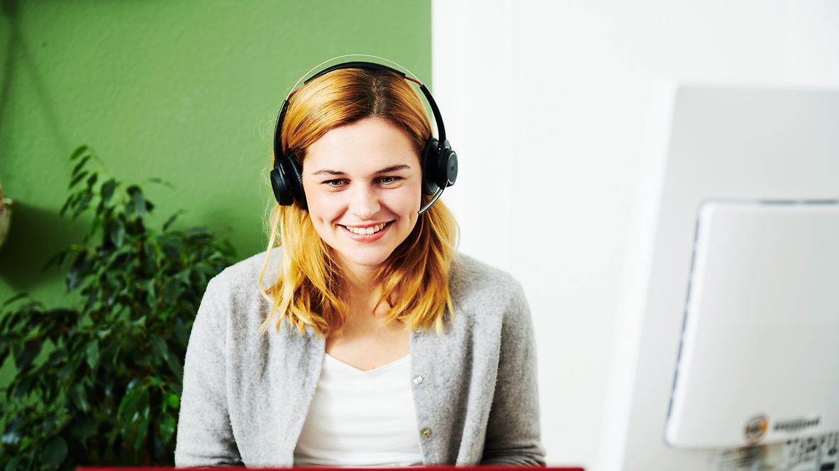 Eine Frau sitzt lachend mit Headset vor ihrem Computer.