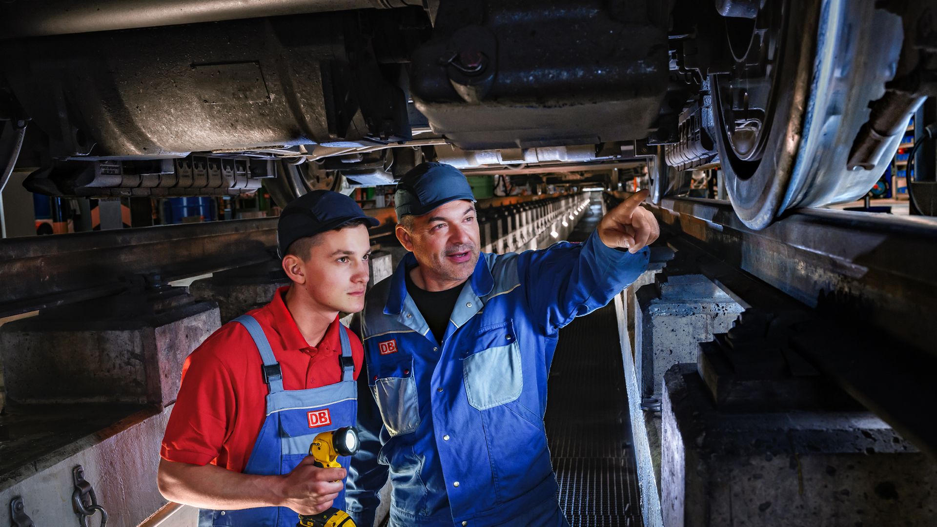 Ein Auszubildender zum Instandhalter und ein Ausbilder stehen in der Wartungsgrube und prüfen die Radsätze eines Zuges