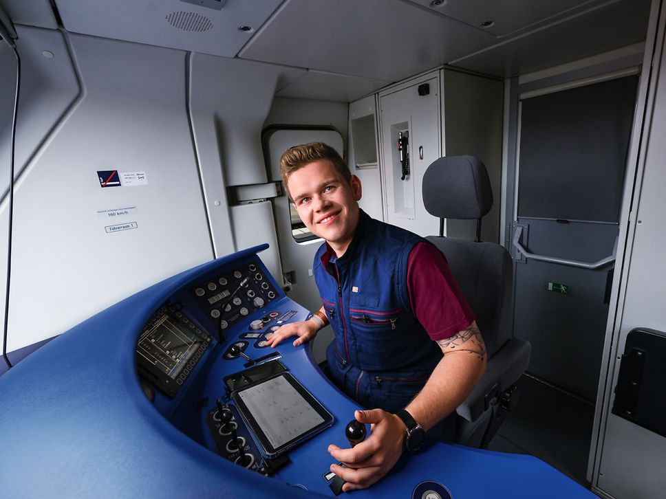 Ein Auszubildender zum Lokführer sitzt in Arbeitskleidung im Führerstand eines Zuges