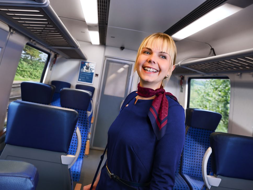 Eine Kundenbetreuerin im Nahverkehr in Unternehmensbekleidung steht im Gang eines Regionalzuges