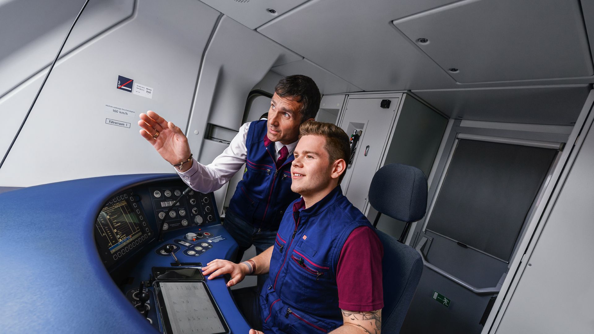 Ein Auszubildender zum Lokführer sitzt neben einem Ausbilder im Führerstand eines Zuges und steuert den Zug