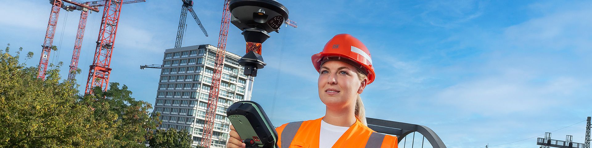 Eine Vermessungsingenieurin läuft in Warnkleidung mit einem GPS-Vermessungsgerät in der Hand auf einer Bahnüberführung