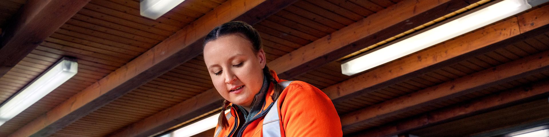 Eine Auszubildende zur Gleisbauerin bearbeitet eine Holzschwelle mit Klopfholz und Beitel