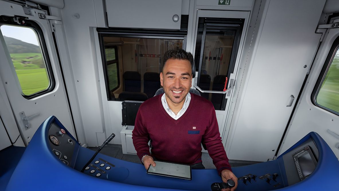 Ein Lokführer sitzt im Führerstand einer S-Bahn und bedient die Steuerung und ein Tablet