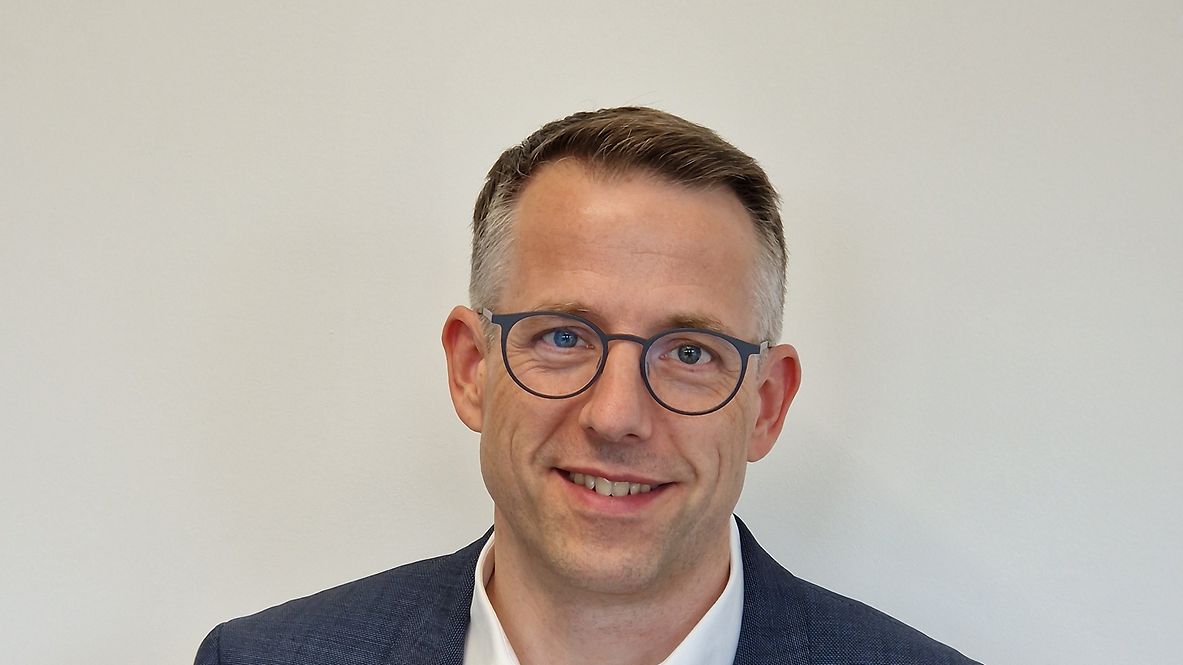 Porträtfoto von Marc Willich, freundlicher Mann in blauem Jacket, vor einem neutralen Hintergrund, trägt ein Brille