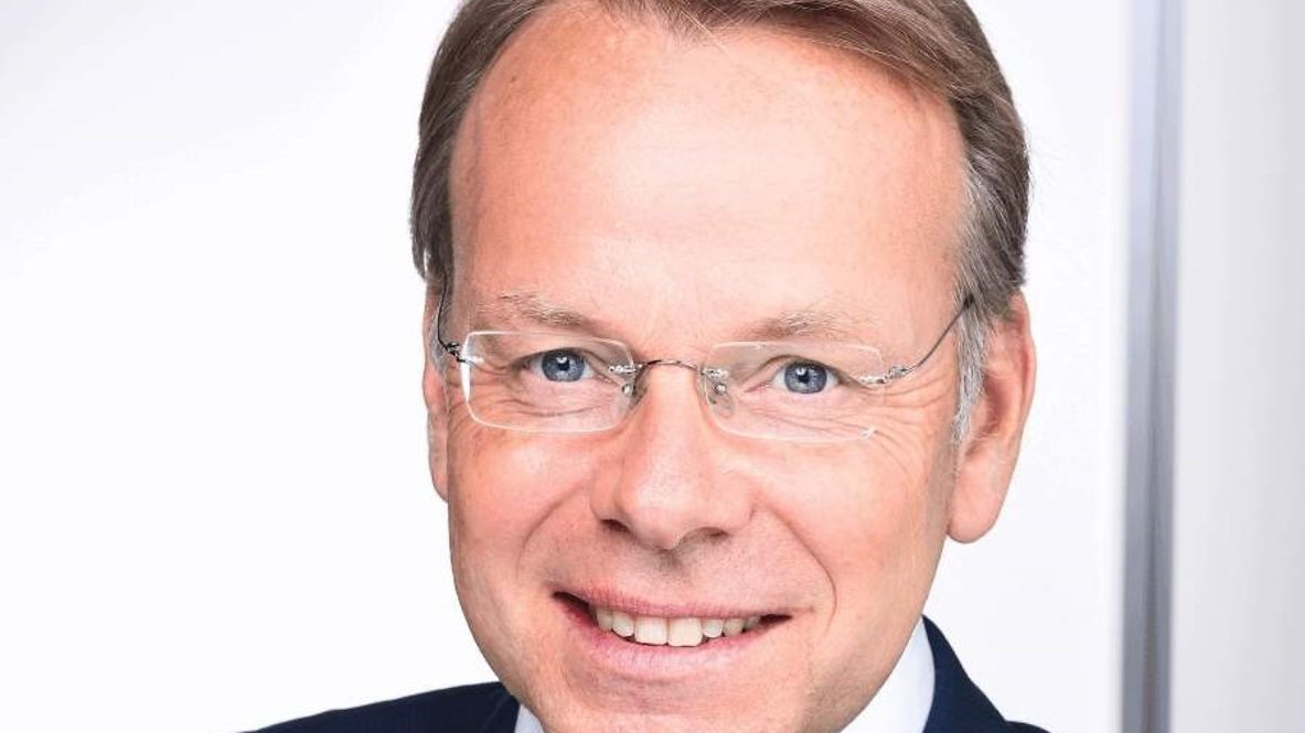 Porträtfoto von Axel Sondermann, freundlicher Mann, vor einem neutralen Hintergrund, trägt eine blauen Anzug und eine Brille