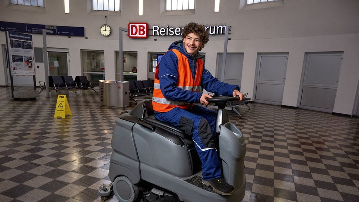 Ein Gebäudereiniger in Ausbildung steuert eine Kehrmaschine in einem Bahnhofsgebäude