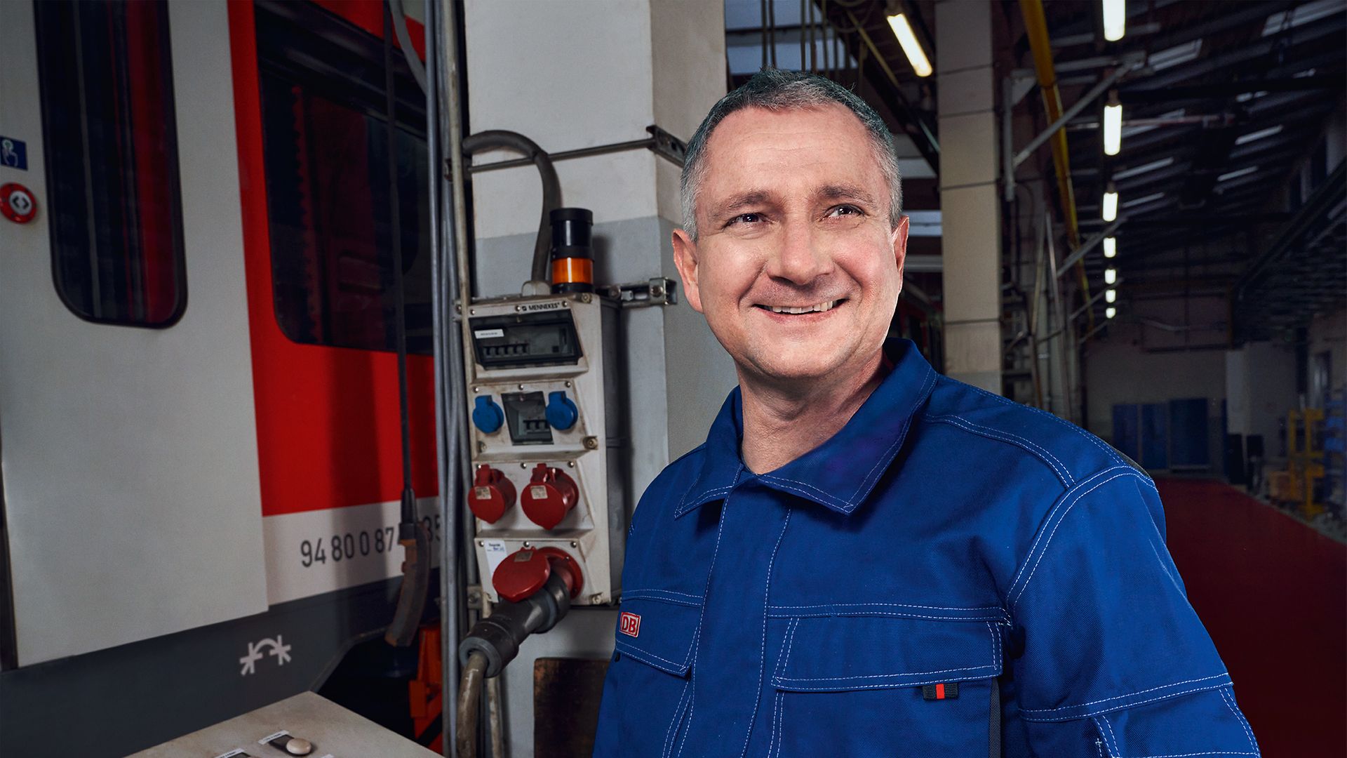 Ein Instandhalter in Arbeitskleidung steht im Werk neben einem Zug und prüft die externen Anschlüsse des Zuges