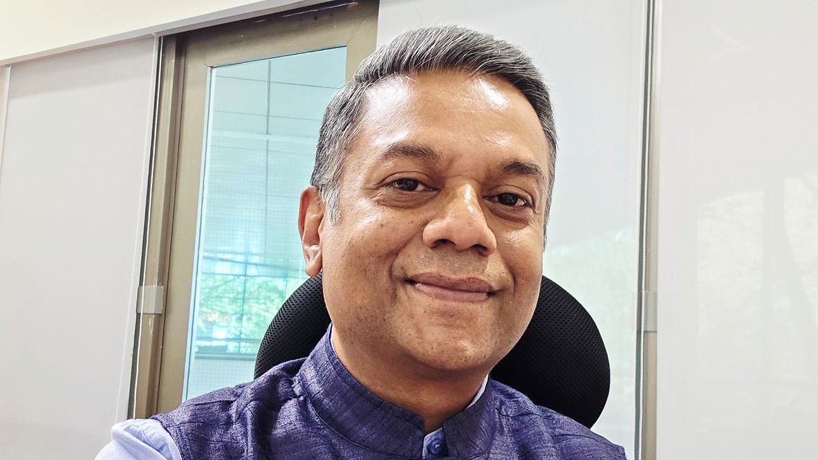 Porträtfoto von Milind Nirmal, trägt eine blaue Weste und ein blaues Hemd, sitzt auf einem Stuhl