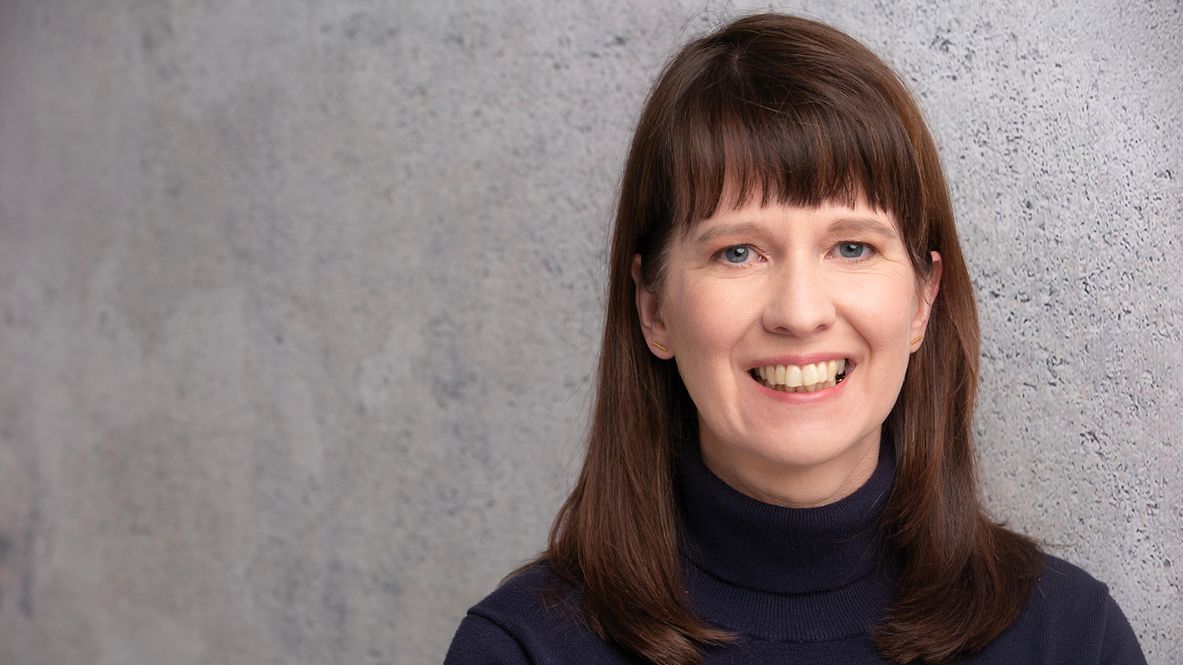 Porträtfoto von Timo Simon, trägt einen beigen Anzug, steht lächelnd in der Natur, hat die Arme verschränkt